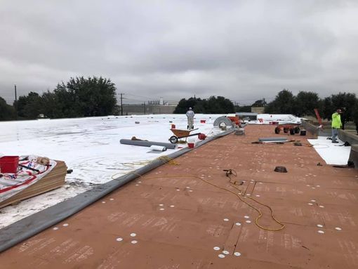 Roofing crew working on a large flat roof, with partially installed white membrane, tools and supplies on site.