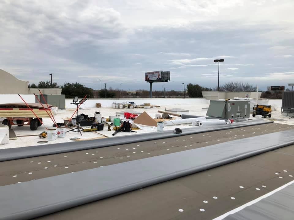 Construction site with finished building, white roof, tan walls, and multiple trucks in front.