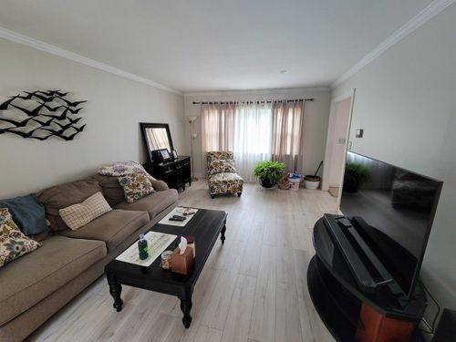 A living room with a brown sofa, black coffee table, patterned armchair, and a television on a stand near the window.