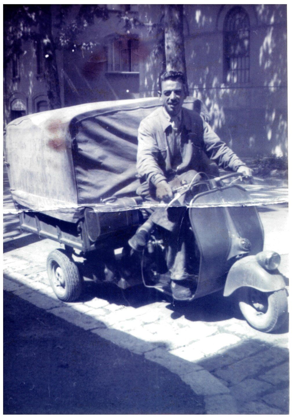 Uomo su una Vespa d'epoca a tre ruote con vano di carico coperto. Parcheggiata su una strada, probabilmente in Europa.