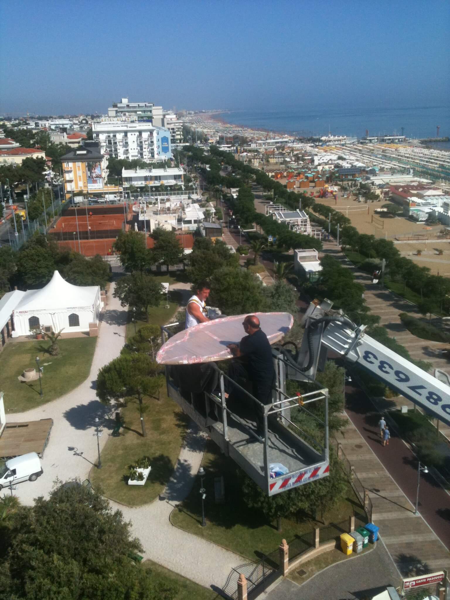 Due persone su un ascensore con una struttura rosa, che domina la città e il mare.