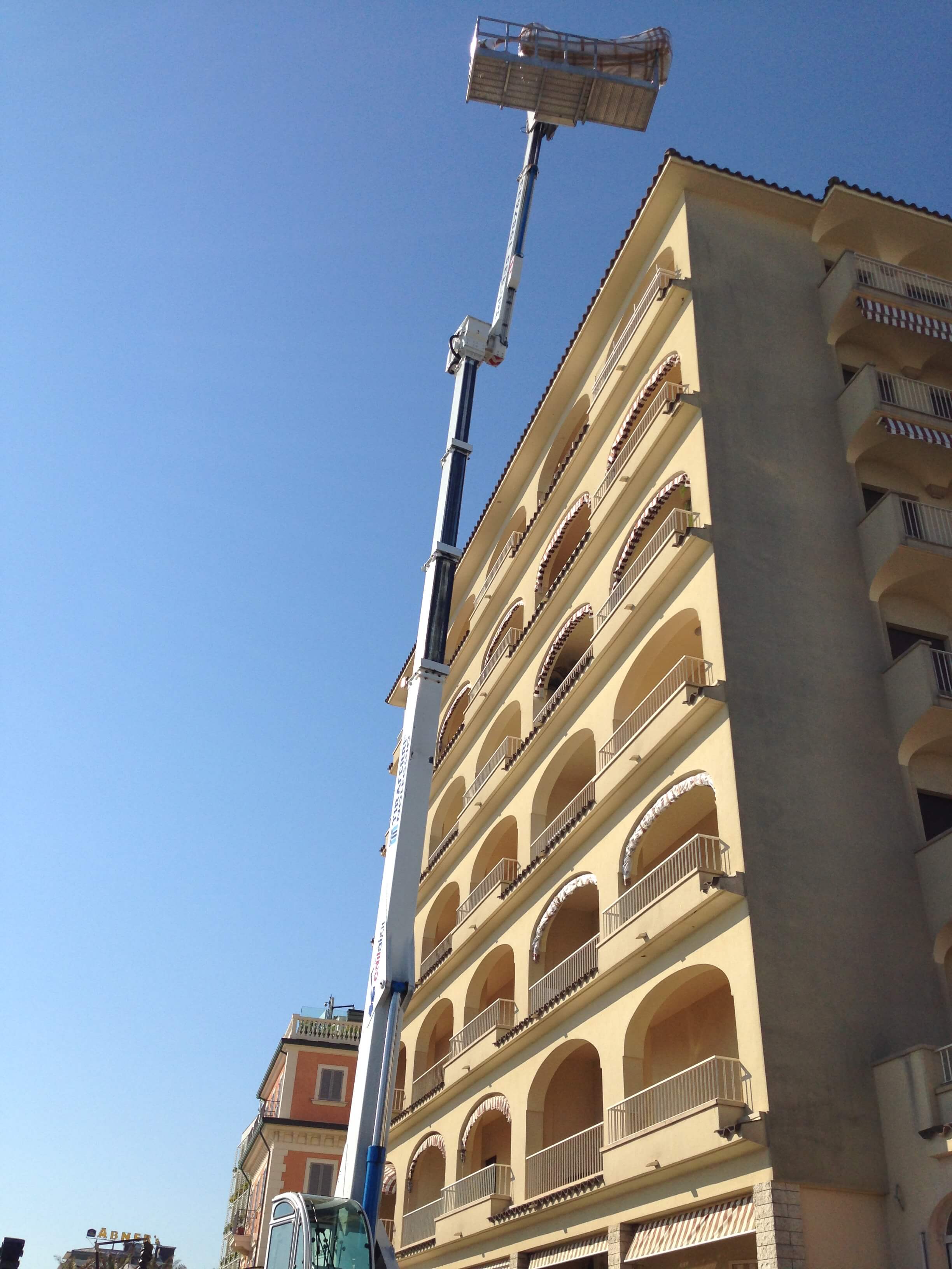 La piattaforma elevatrice blu si estende verso la cima di un edificio. Sono in corso lavori di costruzione o manutenzione.