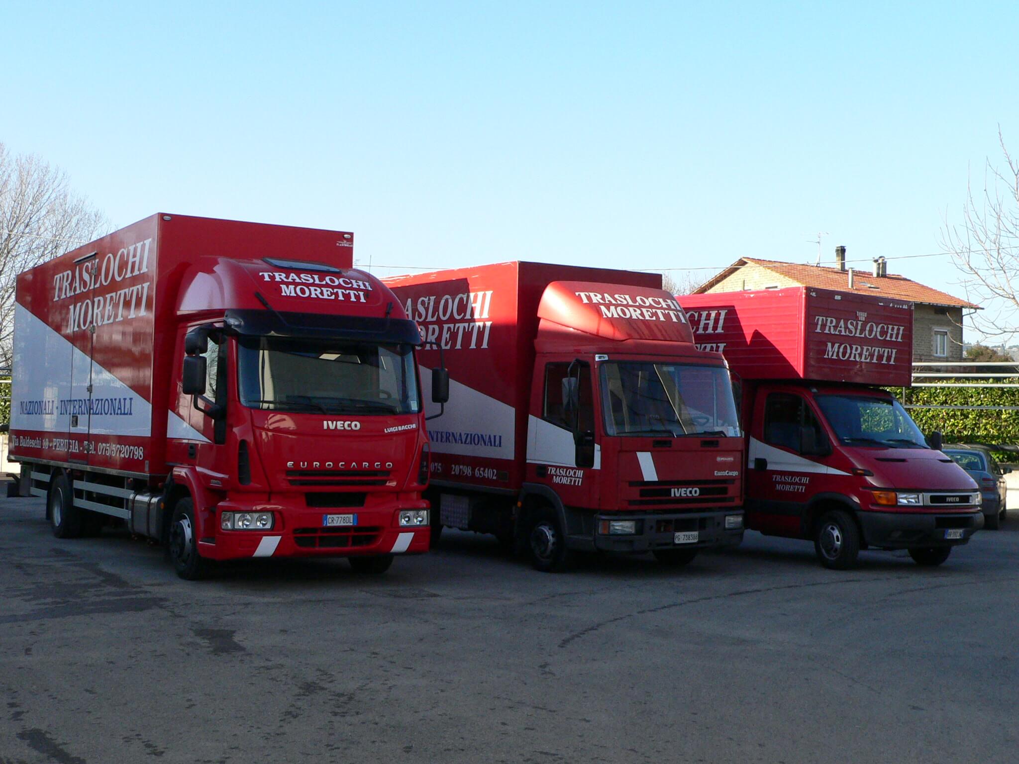 Tre camion dei traslochi rossi e bianchi parcheggiati sul marciapiede sotto un cielo limpido.