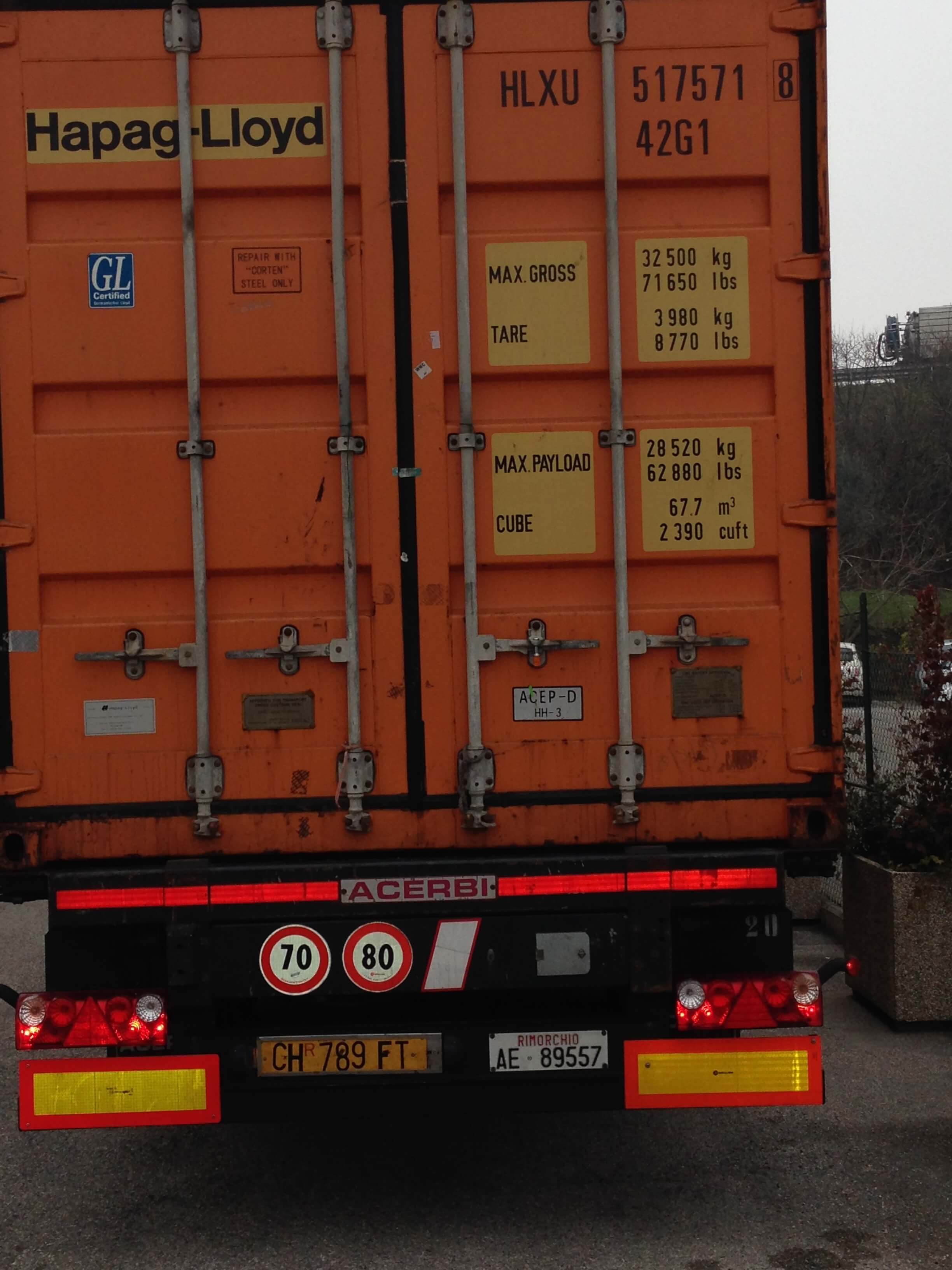 Container arancione Hapag-Lloyd su un rimorchio con cartelli di limite di velocità e targa.