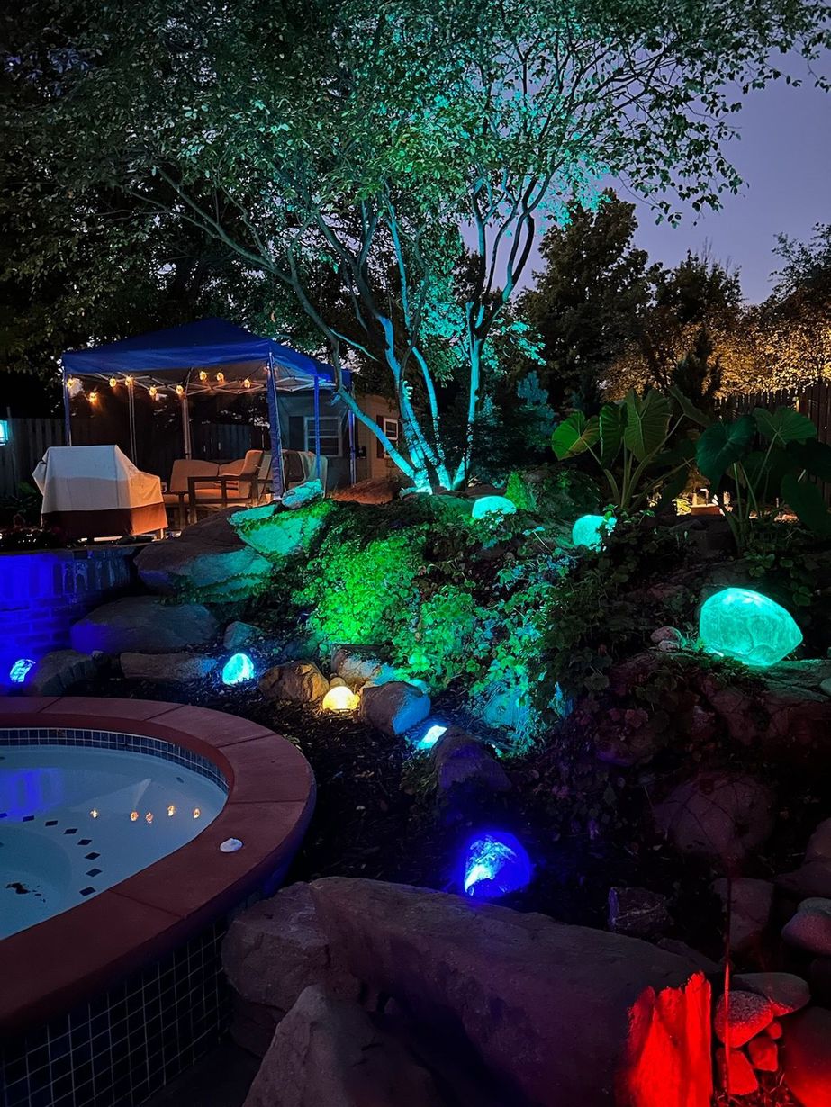 A backyard with a hot tub and trees lit up at night