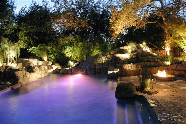 A large swimming pool is lit up at night with purple lights.