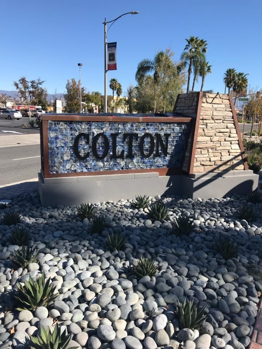 A sign for colton is surrounded by rocks and plants