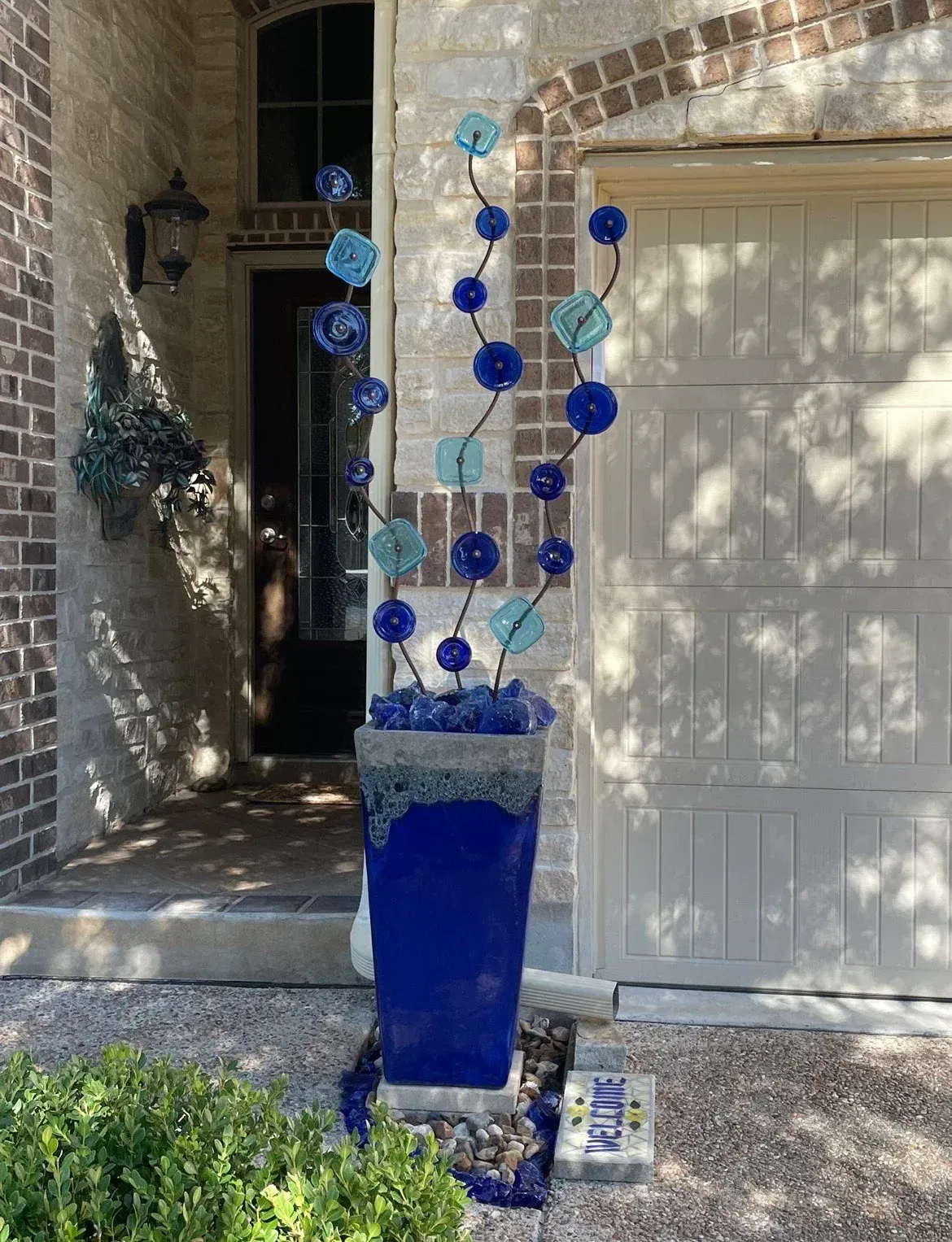 A blue vase with blue flowers is in front of a house.