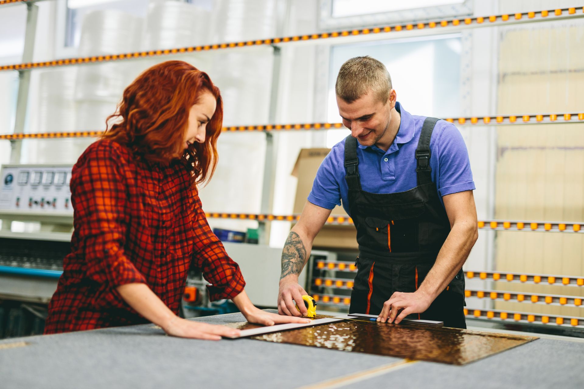 A man and a woman are working on a piece of glass in a factory.
