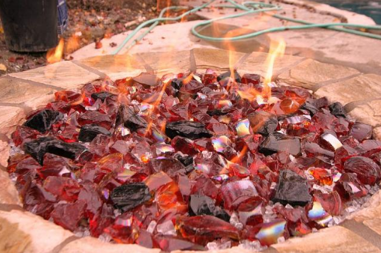 A fire pit filled with red glass and black rocks.