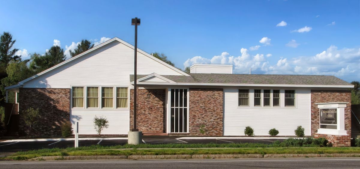 A white and brick building with multiple windows under a blue sky. A tall lamp post is in front of the building.