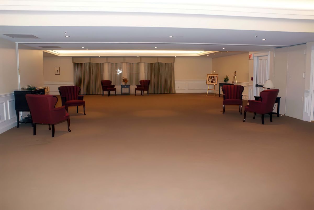 Empty room with burgundy armchairs, brown carpet, and neutral walls.