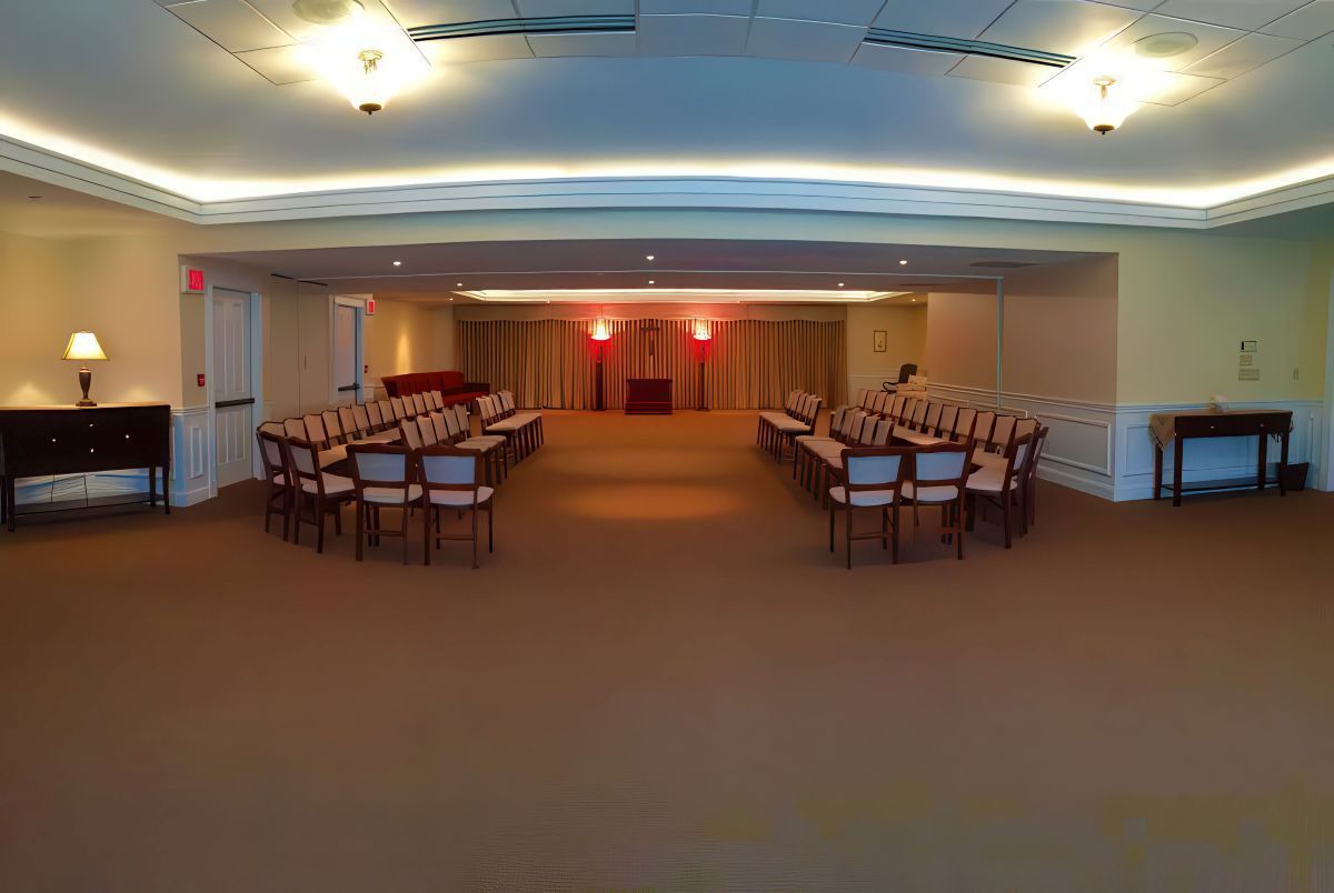 Empty room with chairs arranged in two rows, red lights in the back, tan carpet, and soft lighting.