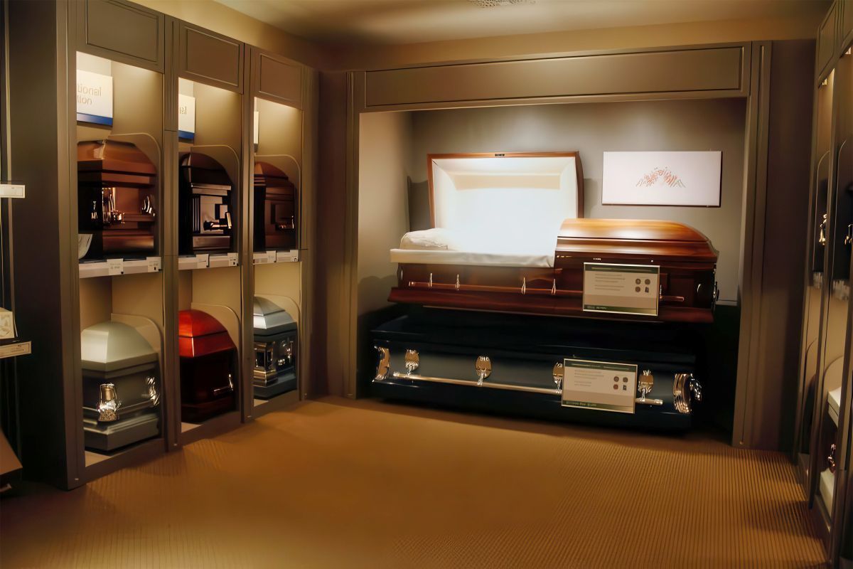 Caskets displayed in a funeral home showroom; various colors and styles, some open.