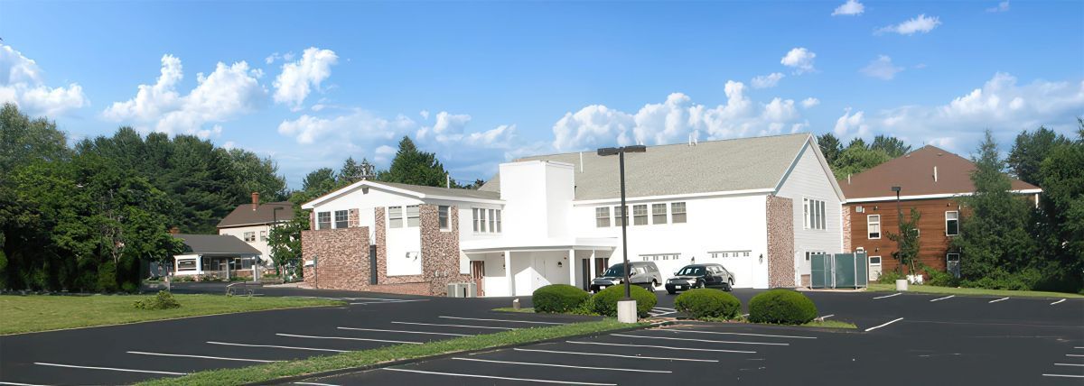 A white and brick building with a parking lot under a blue sky.
