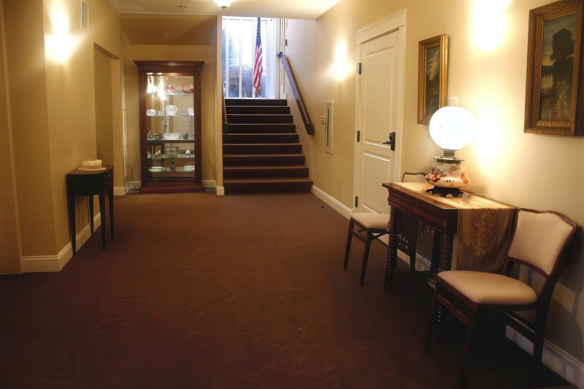 Hallway with stairs and various antique furnishings, including a cabinet, table, and chairs.