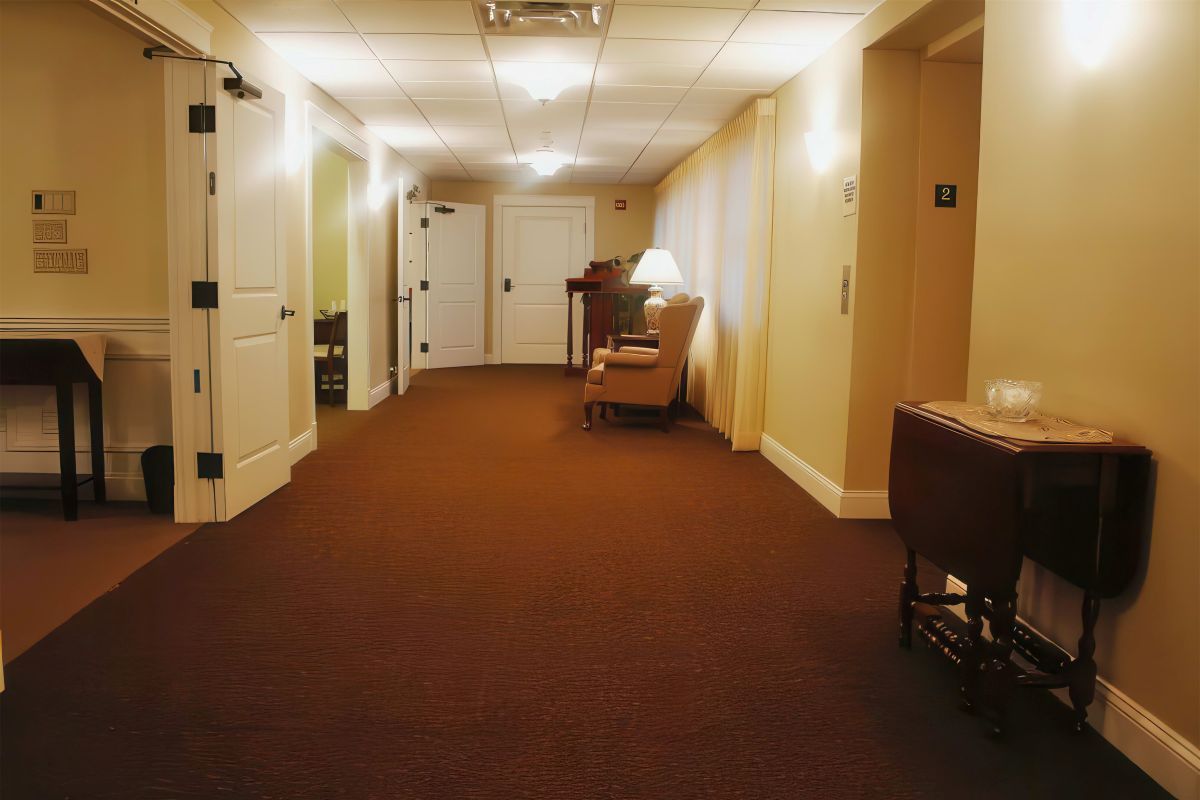 Long hallway with brown carpet, white walls and doors, and various antique furnishings.