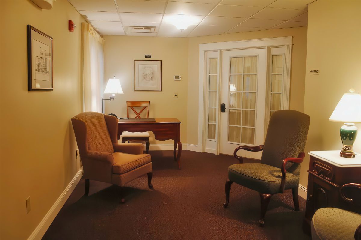 A waiting area with two armchairs, a small desk, and a double door. Brown carpet and beige walls.