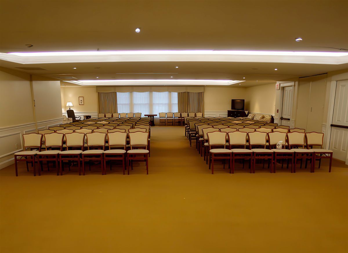 Rows of beige chairs face forward in a large room with a light brown carpet.