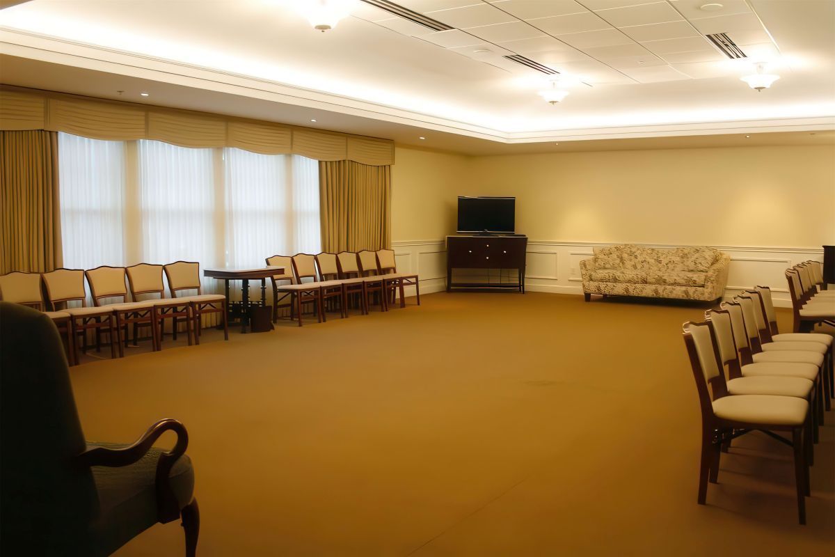 Empty room with rows of chairs, windows with curtains, and a sofa.