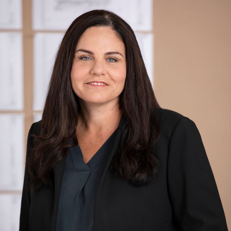 A woman in a black jacket and blue shirt is smiling for the camera.