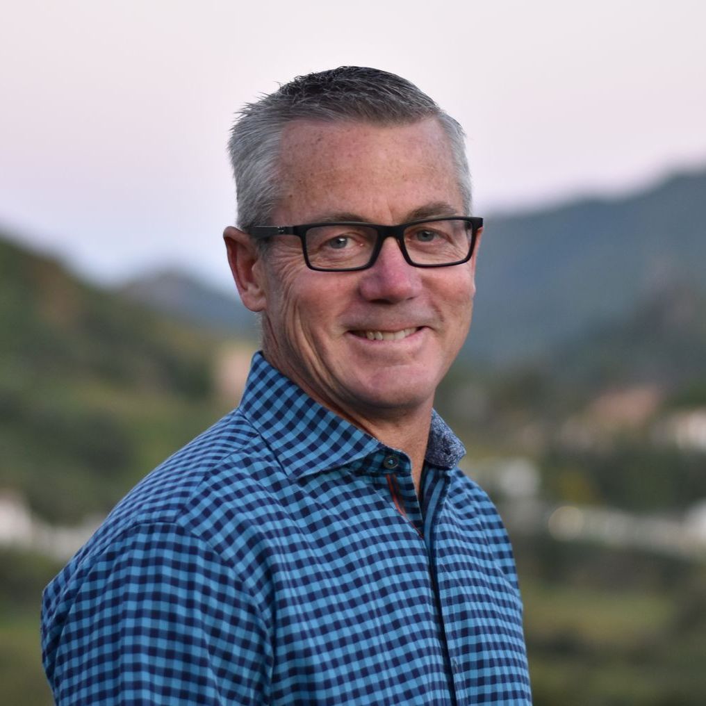 A man wearing glasses and a blue plaid shirt is smiling for the camera.