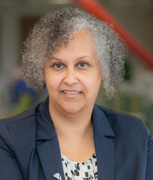 A woman with curly hair is wearing a blue jacket and smiling for the camera.