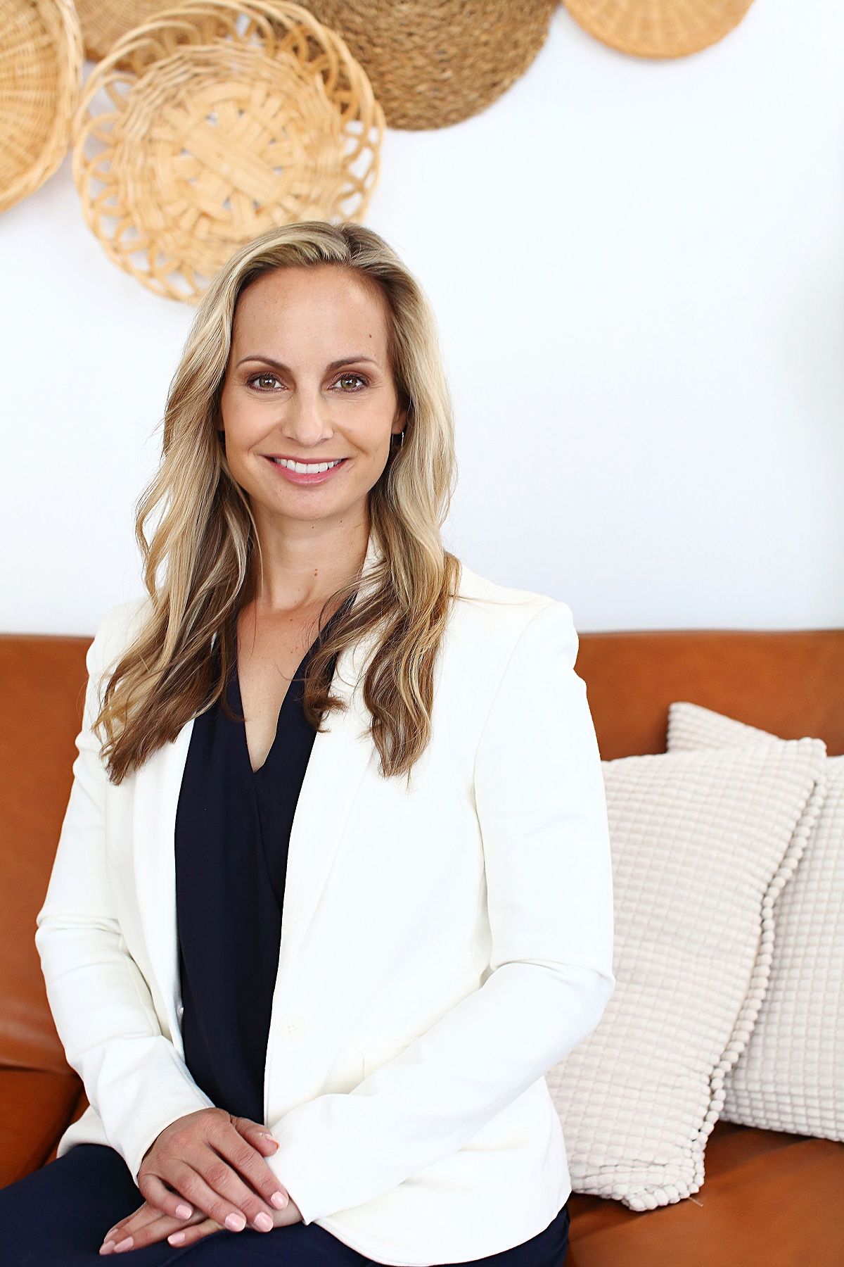 A woman is sitting on a couch wearing a white jacket and smiling.