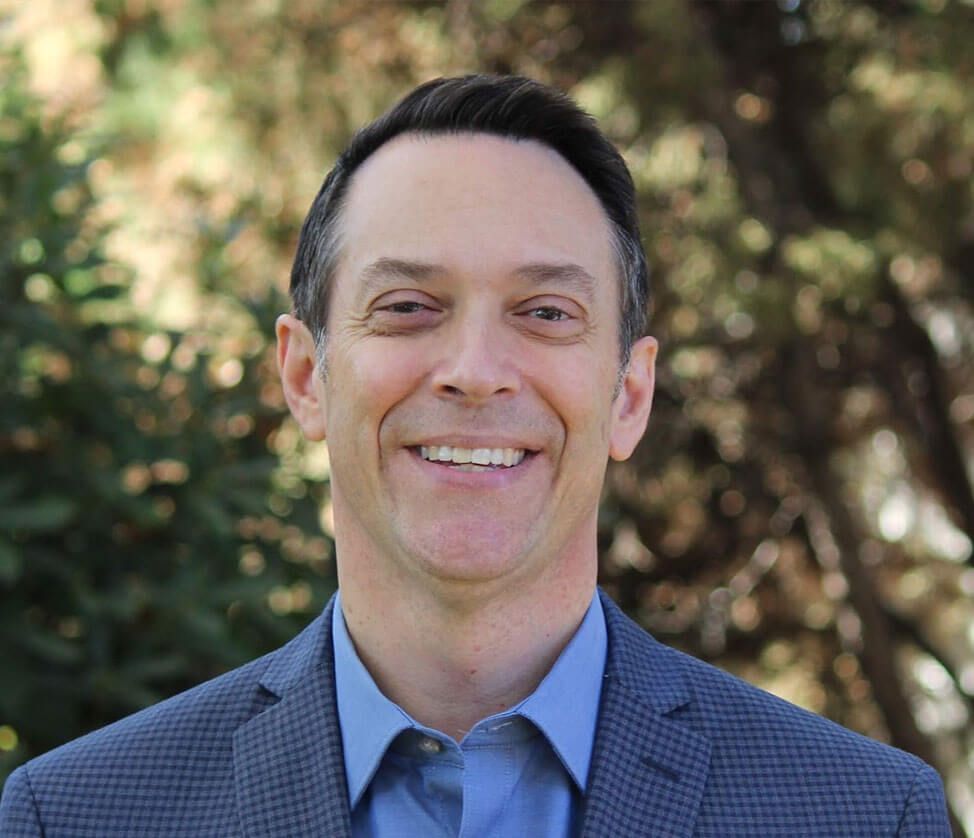 A man in a suit and blue shirt is smiling for the camera.