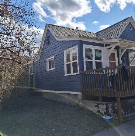A wood-framed home addition under construction attached to the side of a tan vinyl-sided house with two ladders.