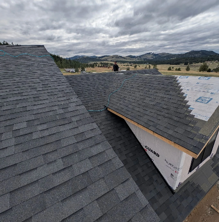 A wood-framed home addition under construction attached to the side of a tan vinyl-sided house with two ladders.
