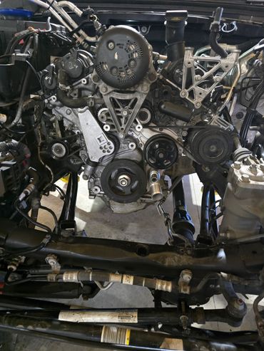 Person washing a car engine bay with a spray bottle, hands visible.