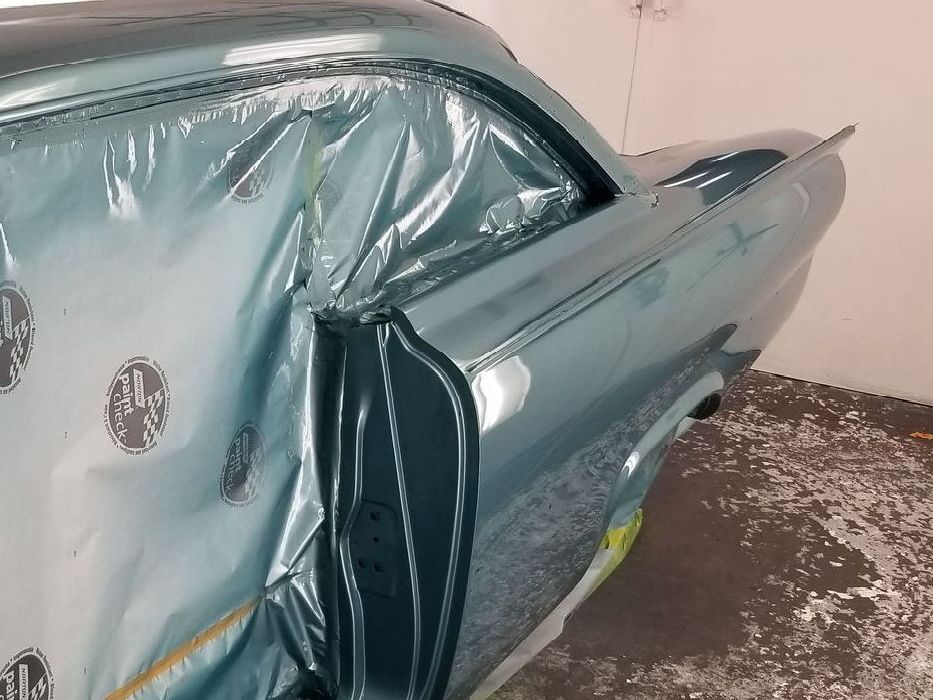 A classic teal car in a spray booth, partially covered in plastic for painting.