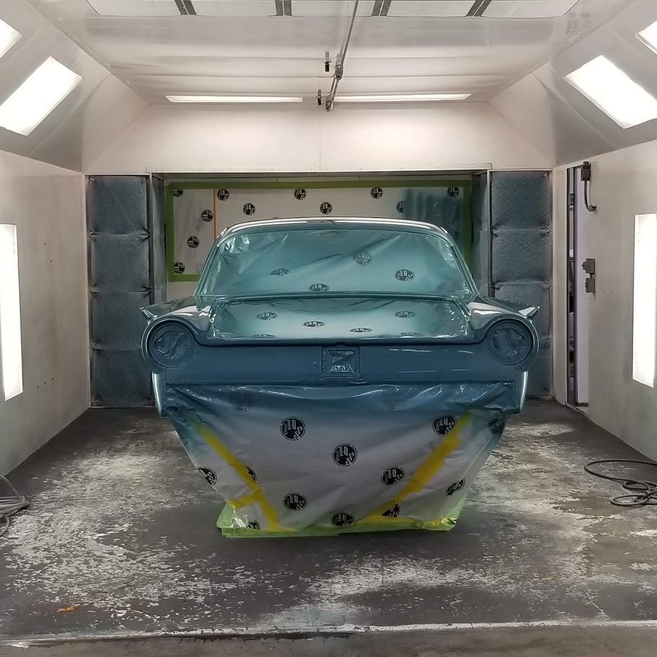 Car in a paint booth, covered in blue plastic and tape, ready for painting.