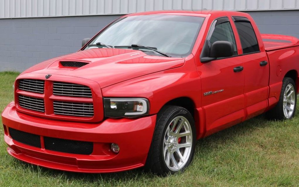 Red Dodge Ram truck with silver wheels on grass.