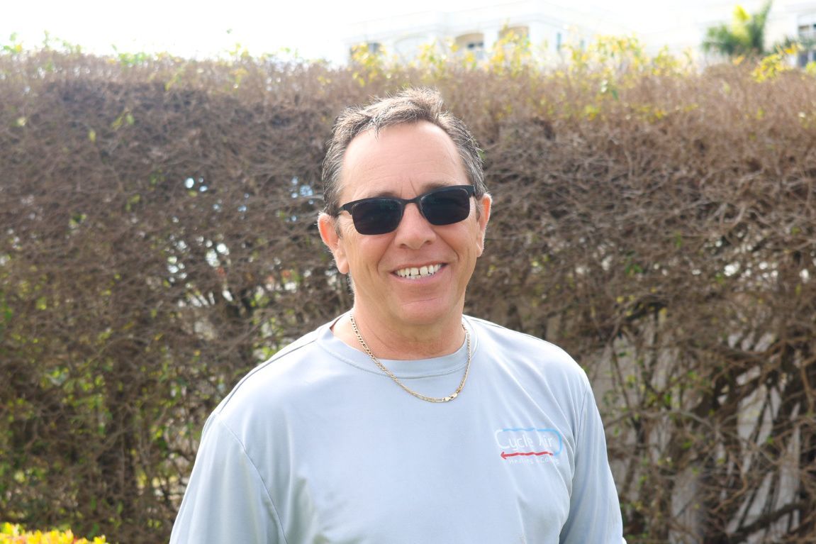 a man wearing sunglasses and a grey shirt smiles for the camera