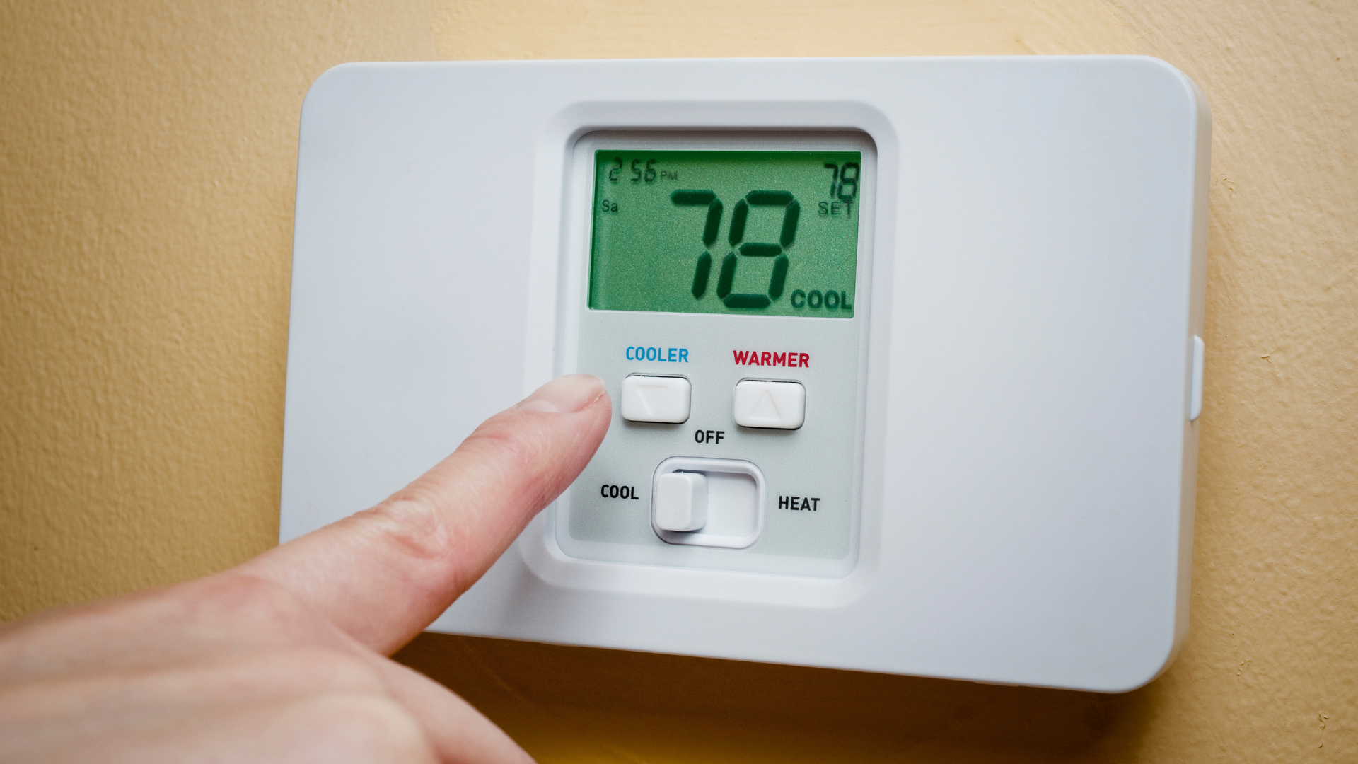 A person is pressing a button on a digital thermostat.