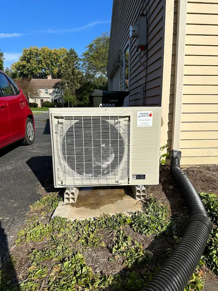 A white air conditioner is sitting on the side of a building next to a red car.
