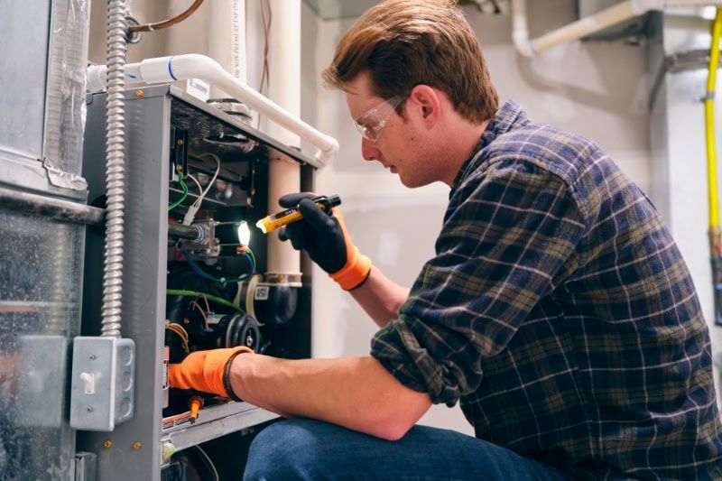 A man is kneeling down and working on an air conditioner.