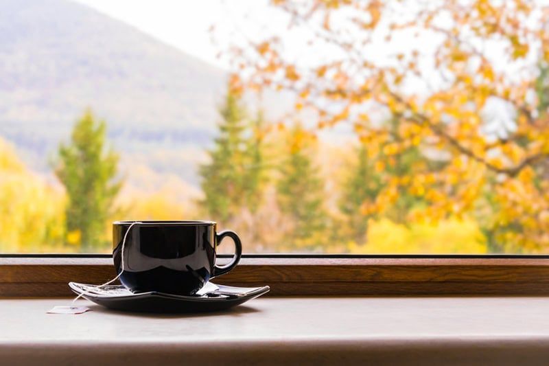 A cup of coffee is sitting on a window sill in front of a window.