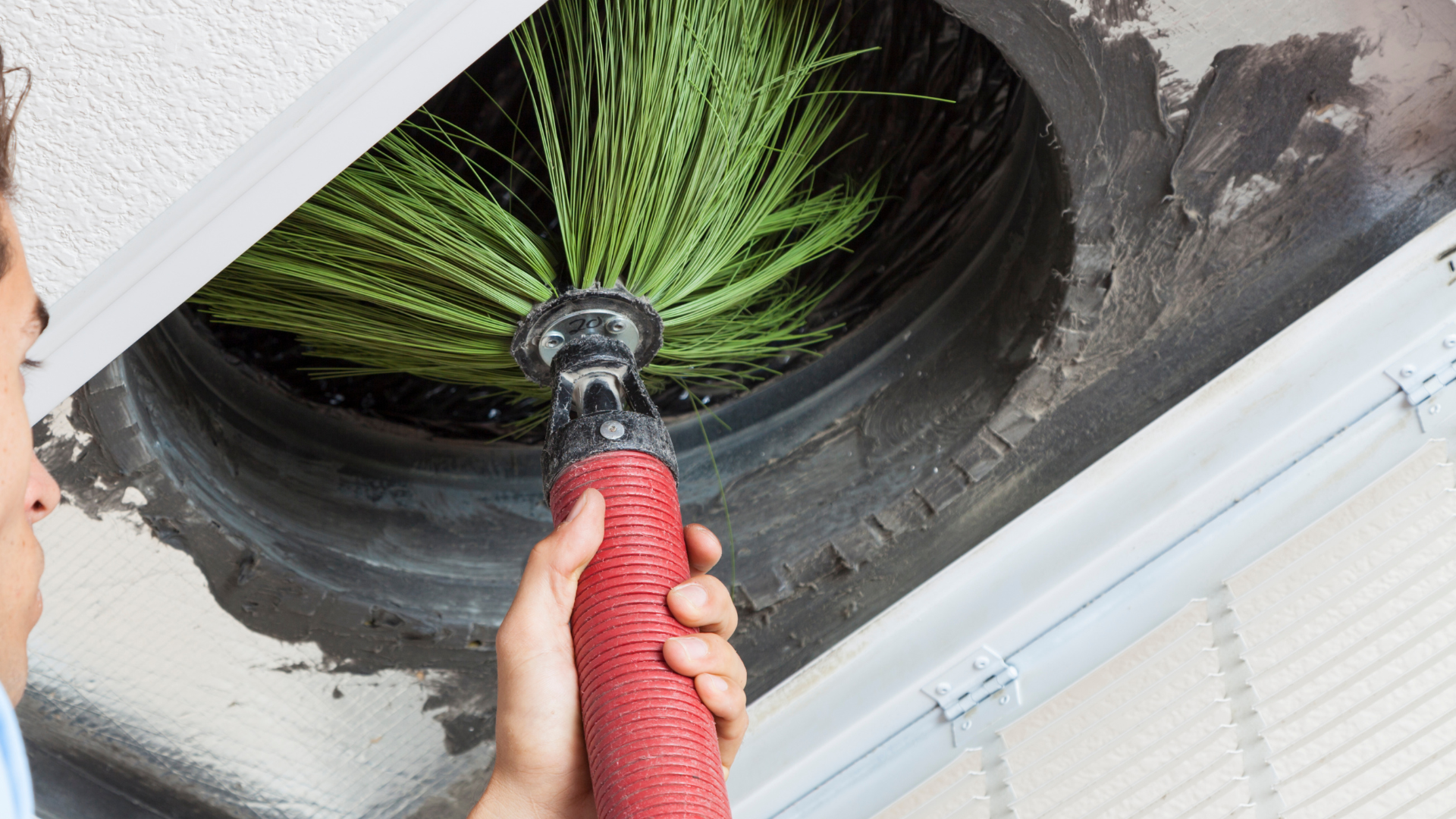 A person is cleaning an air vent with a brush.