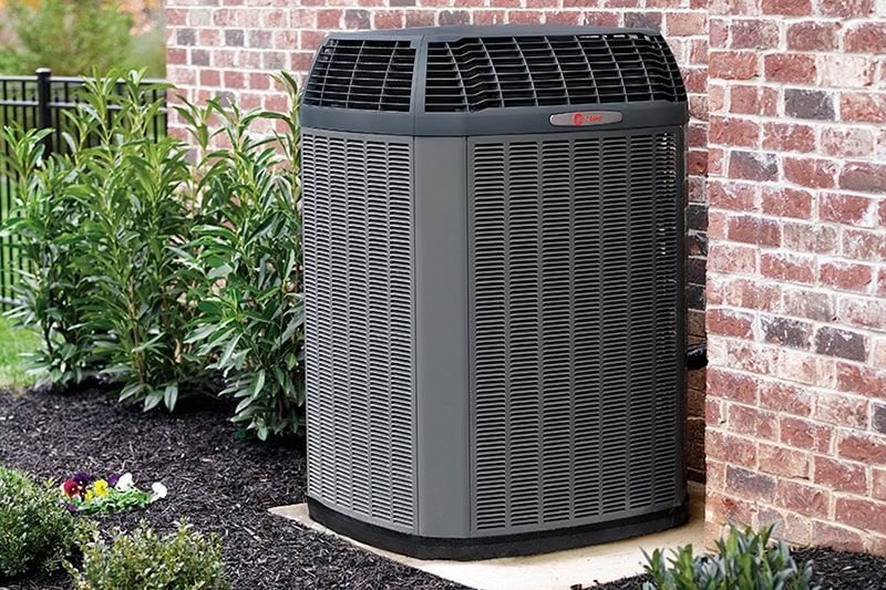 A large air conditioner is sitting on the side of a brick building.