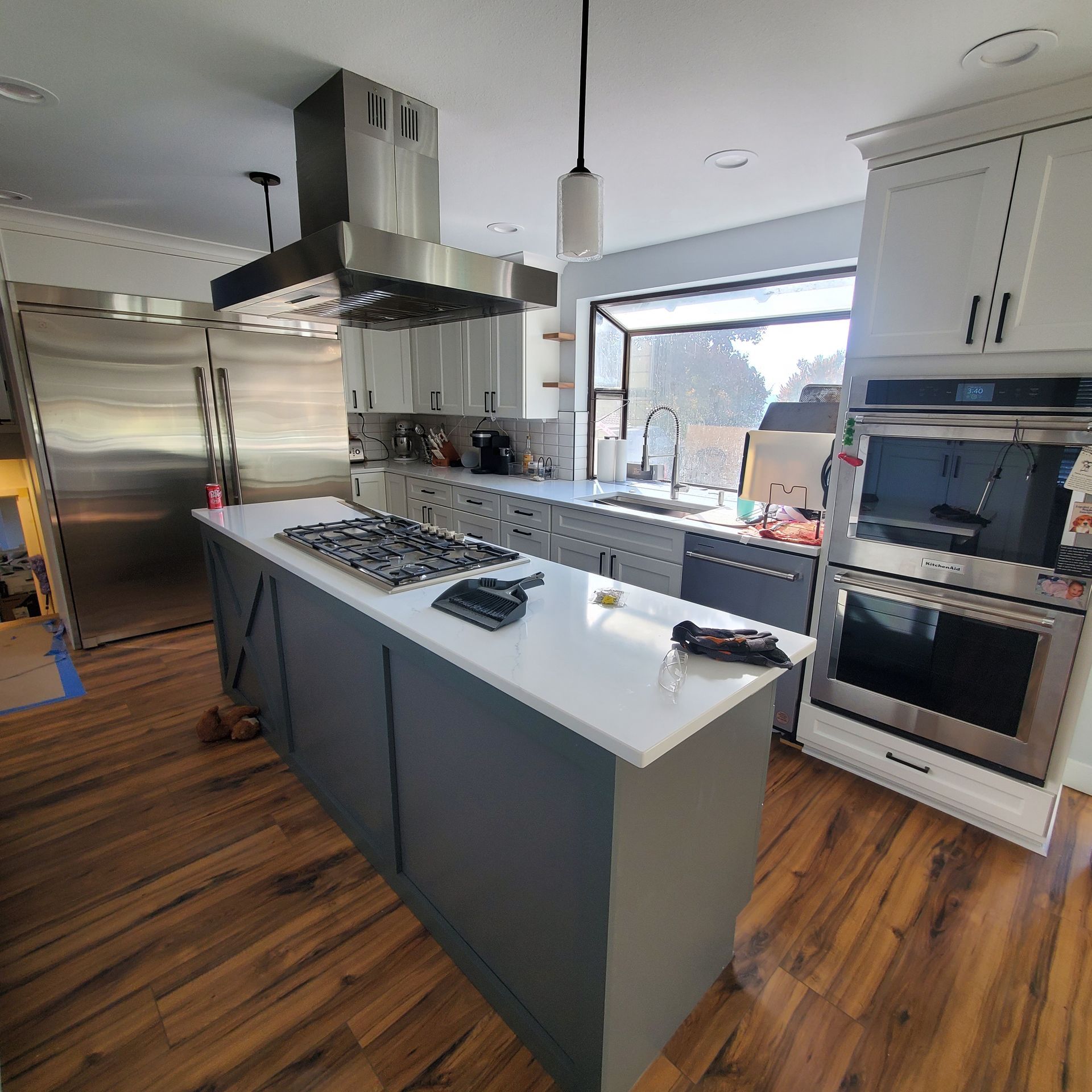 Modern kitchen with island, stainless steel appliances, wood flooring, and large window.