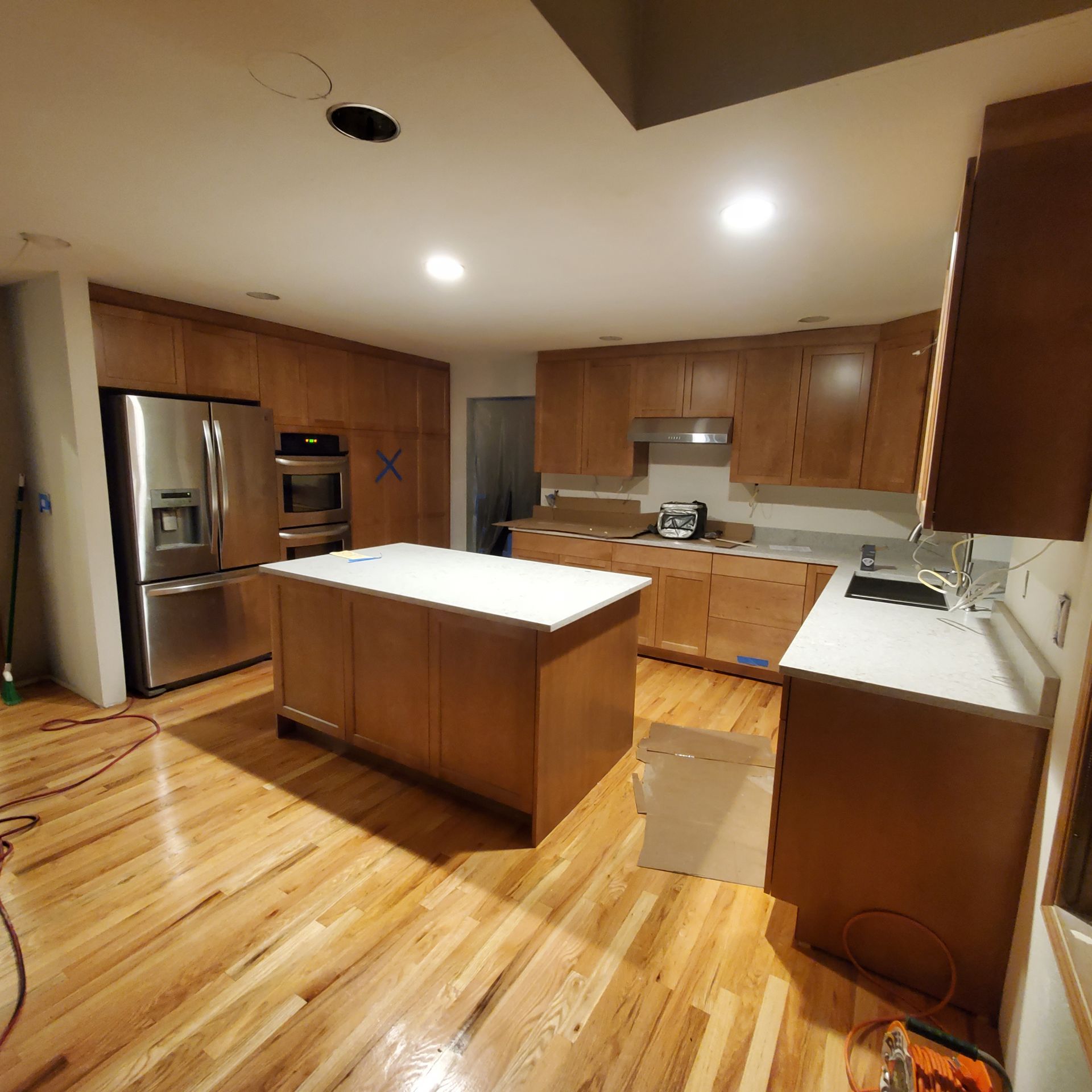 Kitchen undergoing renovation; light brown cabinets, white countertops, stainless steel appliances, and wood floors.