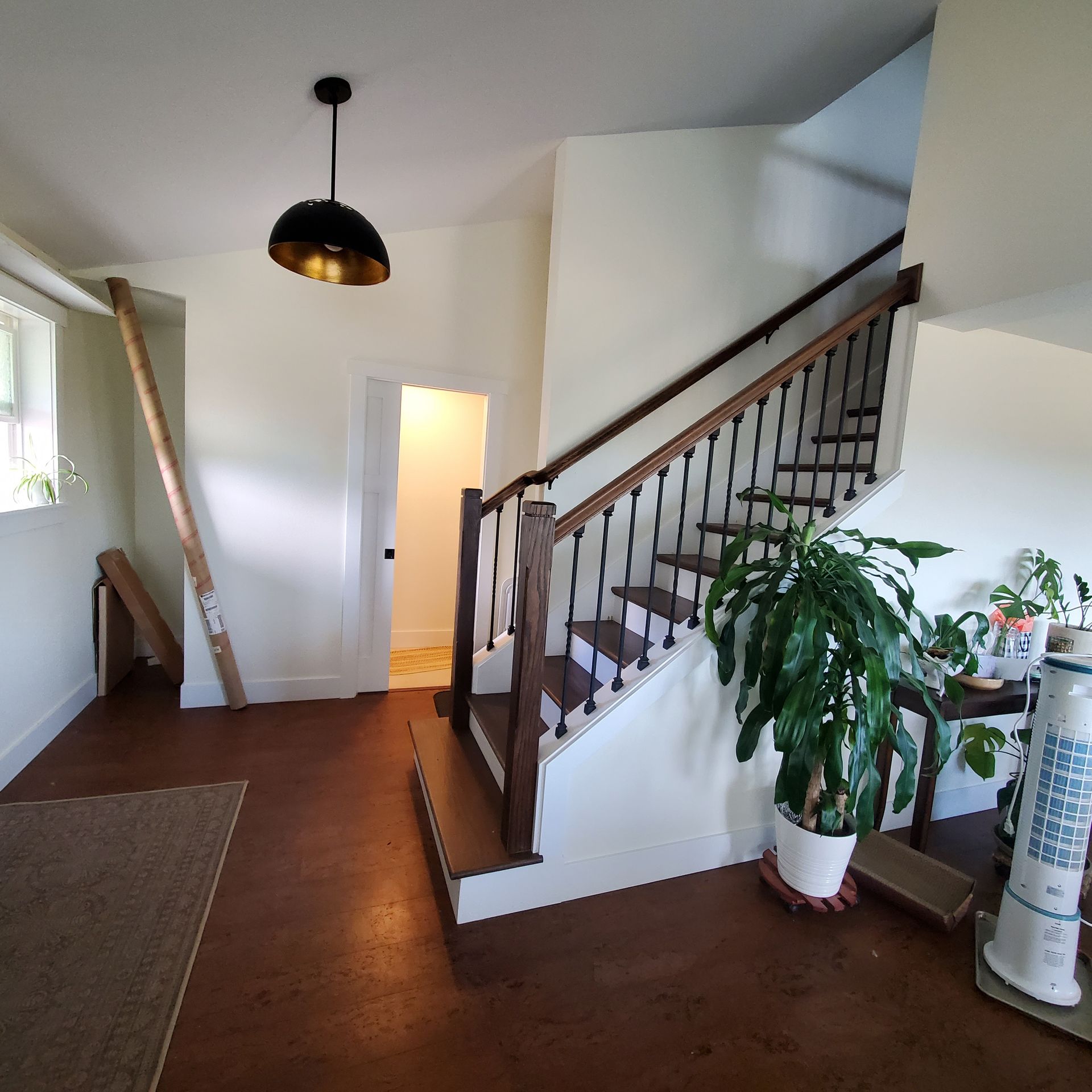 Entryway with staircase, indoor plants, and light fixture, brown floor, white walls.