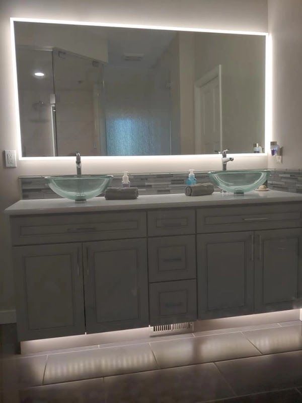 Bathroom with a large mirror with LED lighting, a double sink vanity, and glass vessel sinks.