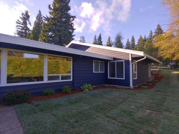 Blue house with white trim and large windows; green lawn and trees.