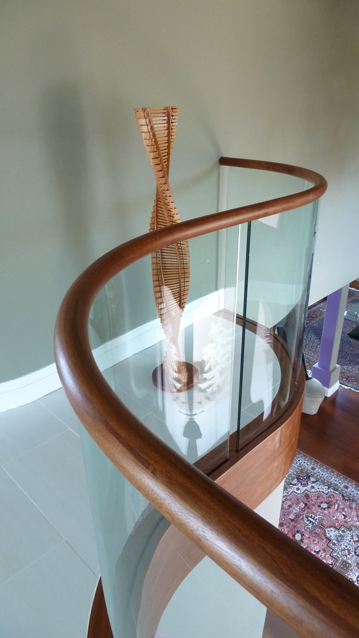 Curved wooden railing with glass panels, holding a tall, decorative wooden sculpture, interior.