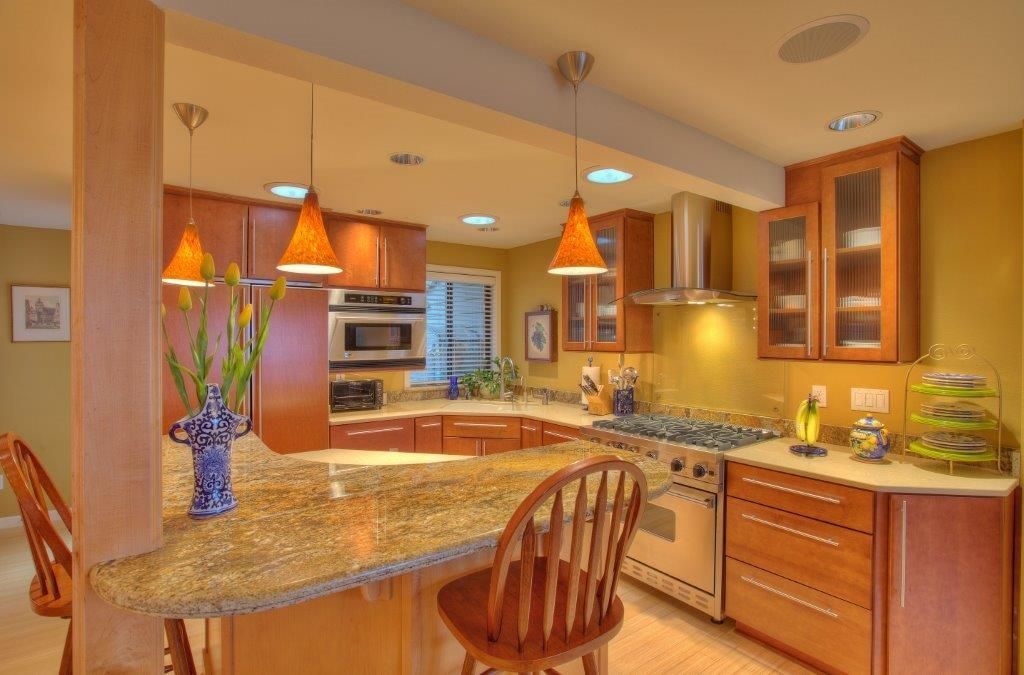 Warm-toned kitchen with wooden cabinets, granite countertop, stainless steel appliances, and pendant lights.