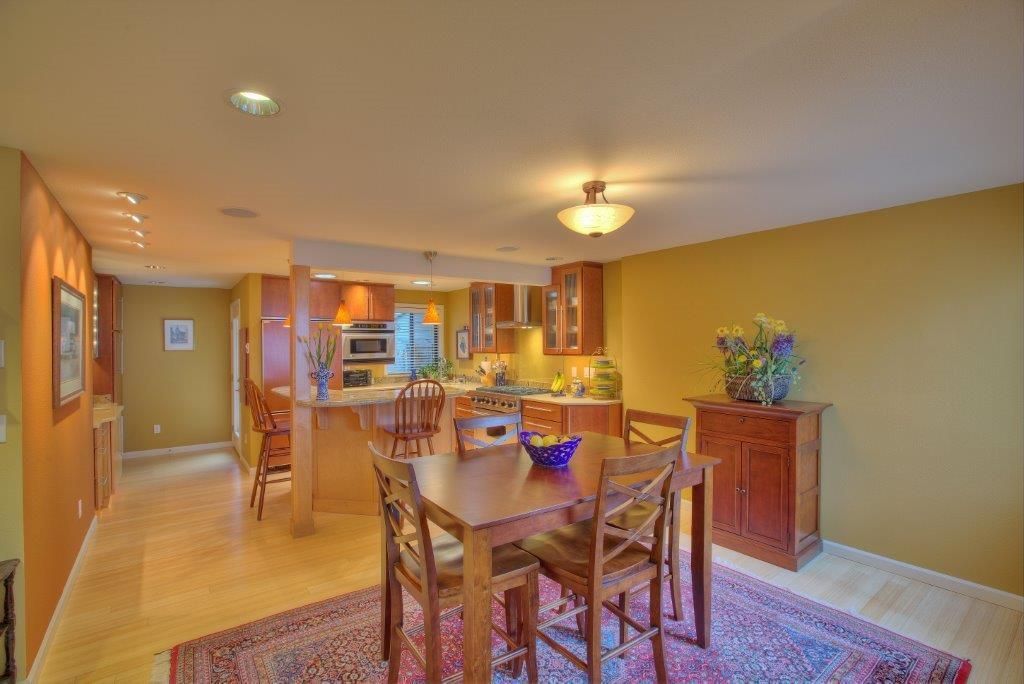 Dining area with a table, chairs, and rug near a kitchen with cabinets and a breakfast bar.